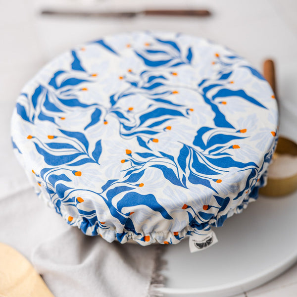 Blue and white patterned dish cover on a white surface with a wooden spoon and white container in the background.