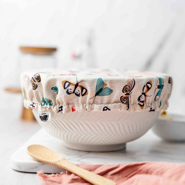 White ceramic bowl with colorful butterfly pattern on a white surface with a wooden spoon and pink cloth.