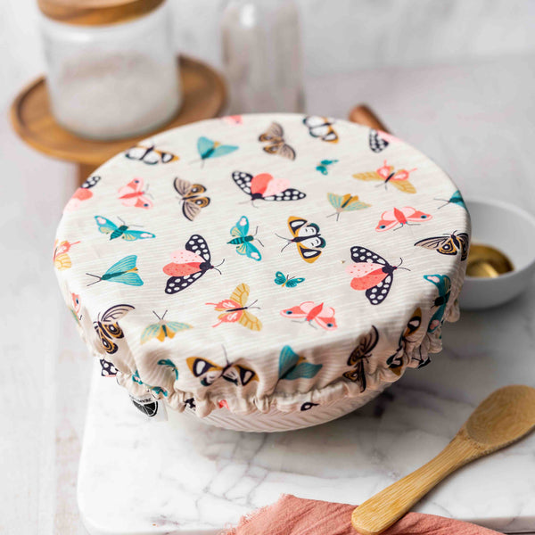 Butterfly-patterned lid on a container with a wooden spoon and pink cloth on a white surface.