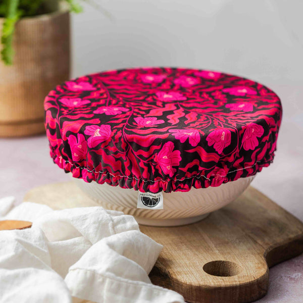 Pink floral-patterned lid on a white container with a wooden cutting board and plant in the background.