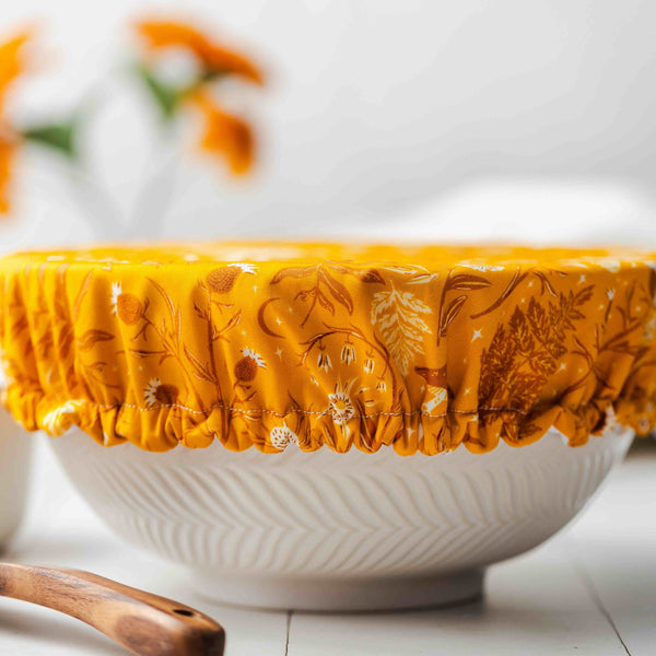 White bowl with a yellow floral-patterned cover on a light wooden surface.