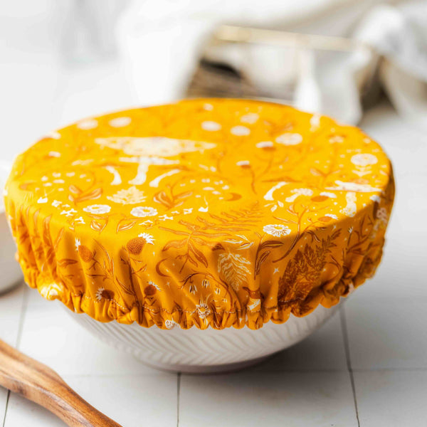 Yellow floral-patterned fabric cover on a white bowl with a wooden tool on a light surface.