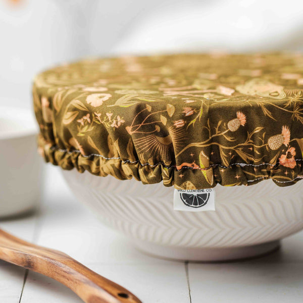 White bowl with a floral-patterned cover on a white surface with blurred flowers in the background