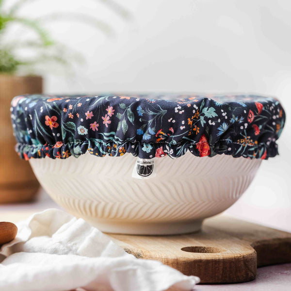 White bowl with floral cover on a white surface with a plant in the background