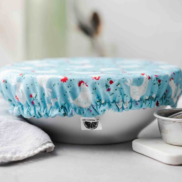 Bowl with a chicken pattern cover on a light surface with kitchen items.