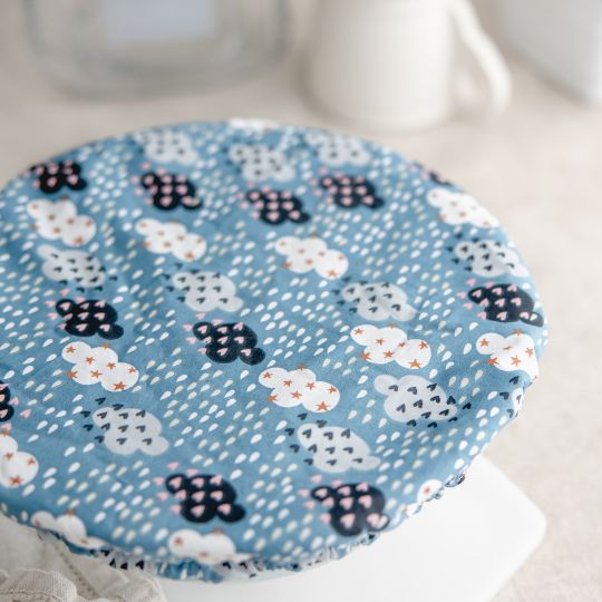 Eco-friendly reusable dish cover, blue with navy, aqua, and white clouds covered in stars and hearts, with raindrops