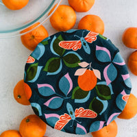 Deep teal reusable bowl cover with moth, clementine, and leaf print