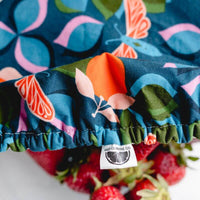 Close up of deep teal reusable bowl cover with moth, clementine, and leaf print