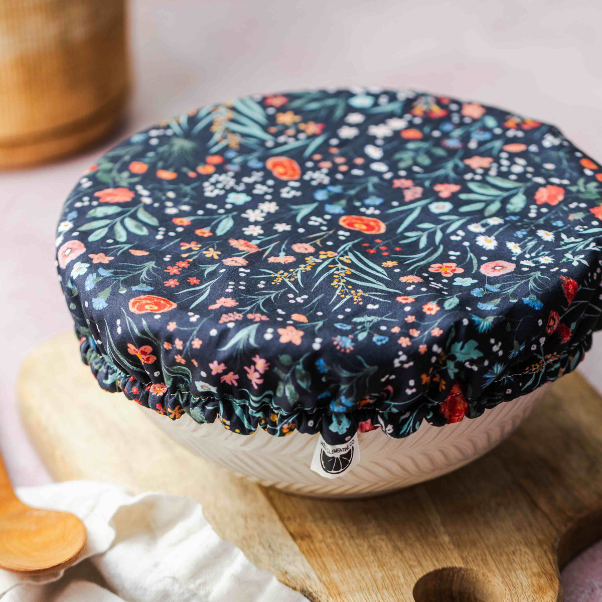 Floral-patterned lid on a white bowl with a wooden cutting board and plant in the background