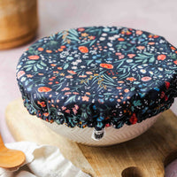 Floral-patterned lid on a white bowl with a wooden cutting board and plant in the background